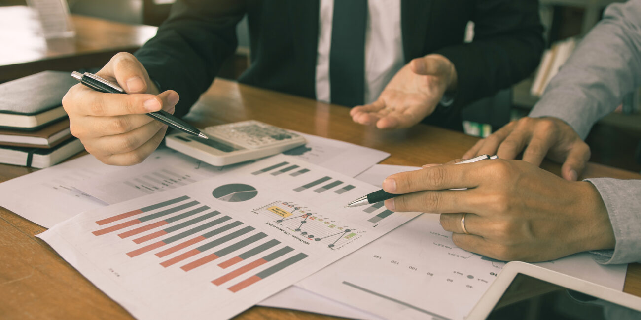 Two businessmen are working analyzing the company annual budget and using digital tablet to find information data result.